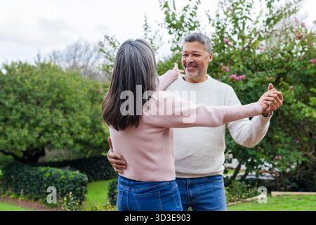 Verschiedene Seniorenpaare tanzen langsam auf grünem Rasen im Garten im Garten mit Pullover und Jeans Stockfoto
