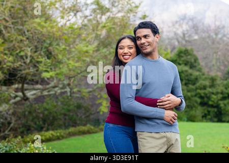 Diverse Paare, die sich auf dem Rasen im öffentlichen Park in burgunderroten und blauen Pullis umarmen, Kopierraum Stockfoto