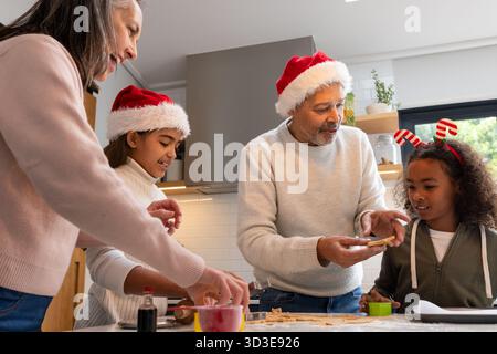 Vielfältige vierköpfige Familie, die auf der Kücheninsel Plätzchenschneider, Urlaubskopfbekleidung backt Stockfoto