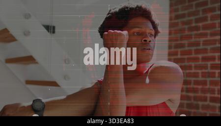 Mann mit rotem Sporthemd und Smartwatch, der zu Hause den Arm über die Brust streckt, mit einer Ziegelwand Stockfoto