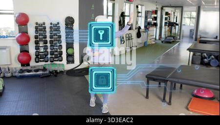 Stehende Erwachsene Frau, die im Fitnessstudio auf AR-Hologramme zugeht, mit weißer Mütze und grauer Leggings Stockfoto