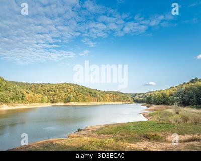 Weiter Blick auf Garasko Jezero in der Nähe von Arandjelovac, Serbien. Der Stausee kurvt zwischen bewaldeten Hügeln mit freiliegender Küste und ruhigem Wasser unter einem hellen Wasser Stockfoto