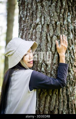 Asiatische Frau umarmt Kiefern. Genießen Sie den Badewald (Shinrin-yoku, mandi Hutan). Gesundheitsmethoden zur Stressreduzierung, Senkung des Blutdrucks Stockfoto