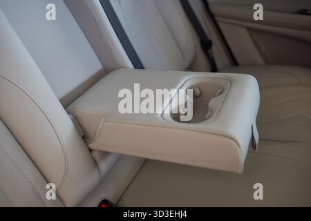 Armlehne mit Getränkehalter innen. Bequeme Beifahrersitze und Armlehne in weiß in Leder. Innenraum aus weißem Leder des modernen Luxuswagens. Modernes Auto Stockfoto