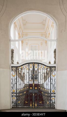 Treppe mit rotem Teppichboden hinter einem kunstvoll verzierten schwarzen und goldenen Eisentor an der Prager Burg. Stockfoto