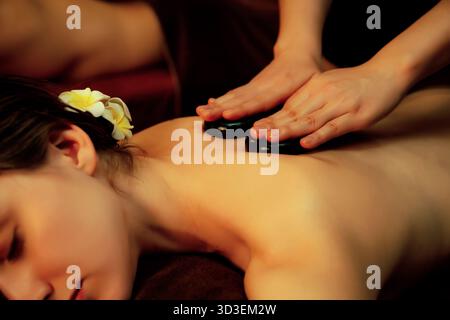 Hot-Stone-Massage im Spa-Salon im Luxus-Resort mit warmem Kerzenlicht, glückselige Paare genießen Spa-Basalt-Stein-Massage gleiten über Körper Stockfoto
