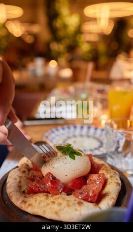 Person, die Bruschetta mit Tomaten zubereitet, Ei auf einer Pizza mit Geschirr Stockfoto