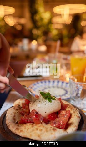 Person, die Bruschetta mit Tomaten zubereitet, Ei auf einer Pizza mit Geschirr Stockfoto
