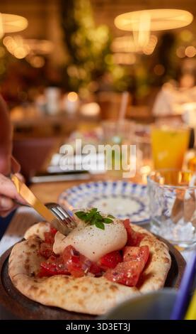 Person, die Bruschetta mit Tomaten zubereitet, Ei auf einer Pizza mit Geschirr Stockfoto