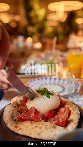 Person, die Bruschetta mit Tomaten zubereitet, Ei auf einer Pizza mit Geschirr Stockfoto