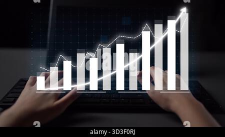 Dieses Bild zeigt ein Paar Hände, die auf einer Tastatur tippen. Auf dem Bildschirm wird ein dynamisches Geschäftsdiagramm angezeigt, das Wachstum und datengesteuerte Daten symbolisiert Stockfoto