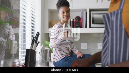 Mit Weinglas, Frau auf Küchenarbeitsplatte, mit Kaffeemaschine, Messerblock, Wasserkocher Stockfoto