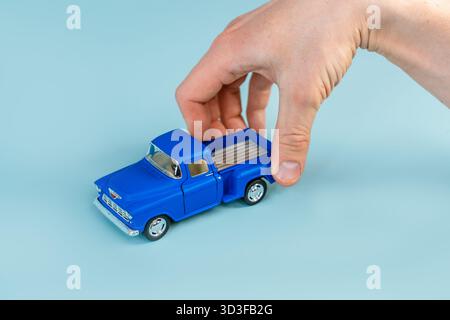 Die Hand eines Mannes hält ein blaues Spielzeugauto auf einem blauen Tischhintergrund. Nahaufnahme, POV-Aufnahme. Stockfoto