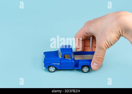 Die Hand eines Mannes hält ein blaues Spielzeugauto auf einem blauen Tischhintergrund. Nahaufnahme, POV-Aufnahme. Stockfoto
