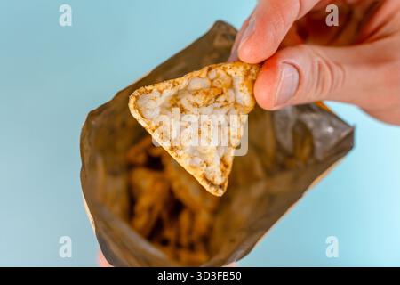 Männerhände essen Maischips Nachos aus einem Paket auf blauem Tischhintergrund. Nahaufnahme, POV-Aufnahme. Stockfoto