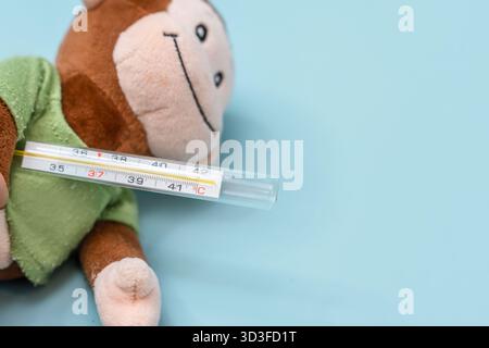 Ein ausgestopftes Affenspielzeug hält ein Thermometer unter seinem Arm, das Konzept der Kinderärzte, auf einem isolierten Hintergrund Stockfoto