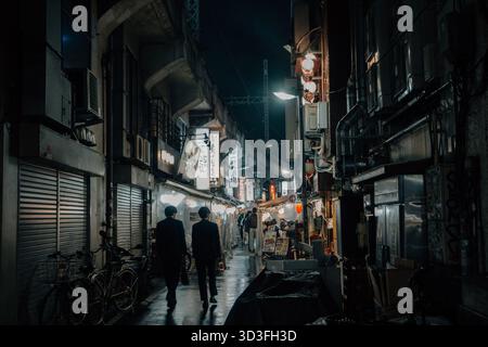 Tokio Hintergasse bei Nacht mit dunkler, düsterer Atmosphäre im Regen mit kleinen Restaurants und Zuggleise darüber Stockfoto