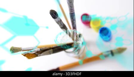 Die Pinsel werden aufrecht im Glasbecher auf dem Studiotisch gezeigt, mit digitalen Farbtöpfen Stockfoto