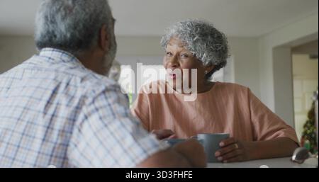 Ein plauderndes Paar mit Lachsbluse an der Küchentheke und Kaffeetassen neben einer Brille Stockfoto