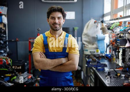 Arbeiter in Arbeitskleidung steht mit gekreuzten Armen in der Werkstatt Stockfoto