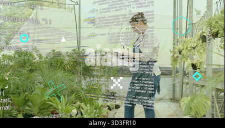 Tablettenhalter, Gartenbauarbeiter, die Topfpflanzen im Gewächshaus überwachen, mit Datenüberlagerung Stockfoto
