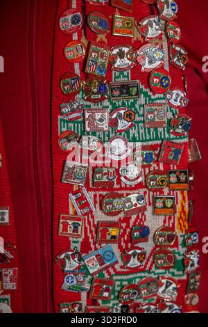 Eine detaillierte Nahaufnahme des Halstuchs eines Liverpool FC Supporters, verziert mit einer Reihe von Emailnadeln, Abzeichen und Patches, die von einem engagierten Fan gesammelt wurden. Stockfoto