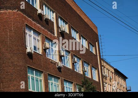 Altes Industriebausteingebäude mit Glasblocktreppe und mehreren externen Klimaanlagen entlang der Fassade. Das Foto zeigt Stockfoto