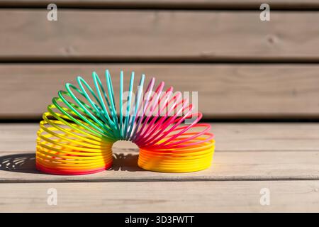 Eine leuchtende, regenbogenfarbene magische Feder, die sich auf einer Holzoberfläche erstreckt, fängt Sonnenlicht ein und zeigt einen lustigen, verspielten Look. Ideal für Themen von ch Stockfoto