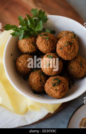 Eine Nahaufnahme knuspriger frittierter Snacks, wunderschön in einer weißen Schüssel auf einem Holzbrett angeordnet. Garniert mit frischer Petersilie, ist dieser appetitliche Snack Stockfoto