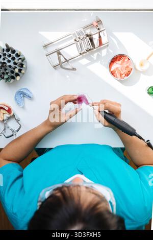 Draufsicht, beschnittene, nicht erkennbare Zahntechnikerin, die sorgfältig eine Zahnprothese herstellt und Präzision in der Zahnarbeit und im Labor zeigt Stockfoto