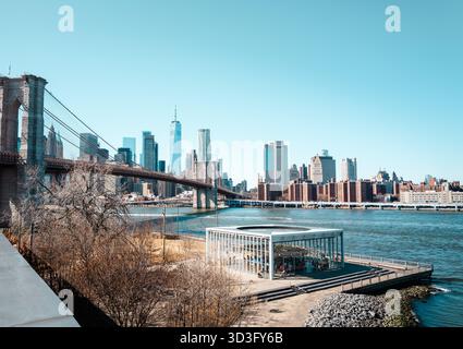 Ein ikonischer Blick auf die Brooklyn Bridge, die sich über den East River erstreckt, mit Manhattans Skyline im Hintergrund an einem sonnigen Tag in New York City. Stockfoto
