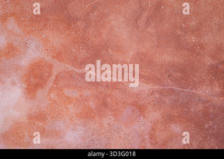 Nahaufnahme einer strukturierten Steinoberfläche mit erdroten Tönen und natürlichen Mustern. Die Oberfläche zeigt subtile Farbvariationen und robuste Texturen Stockfoto