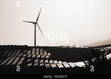 Eine ruhige Landschaft mit einer großen Windkraftanlage, ergänzt durch Reihen von Solarpaneelen, die den Übergang zu erneuerbarer Energie und nachhaltiger Energie symbolisieren Stockfoto