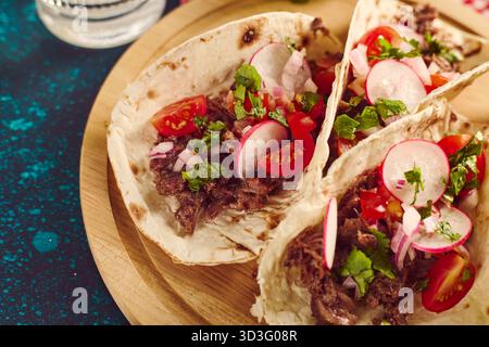 Eine köstliche Nahaufnahme authentischer mexikanischer Tacos gefüllt mit zartem Fleisch, Radieschen, Koriander und Kirschtomaten, die das pulsierende Co einfangen Stockfoto