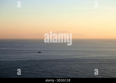 Ruhiger Sonnenaufgang über dem weiten Horizont in Galicien, Spanien, mit einem einsamen Fischerboot. Das ruhige Wasser und die warmen Farben sorgen für eine ruhige Morgensaison Stockfoto