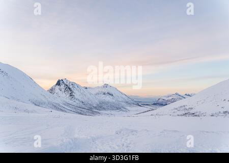 Ruhige Winterlandschaft in Rekvik, Tromso, Norwegen. Schneebedeckte Berge und sanfte Pastellfarben beim Sonnenaufgang schaffen ein ruhiges und atemberaubendes NOR Stockfoto