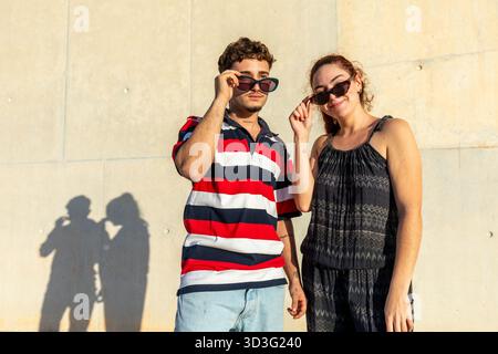 Ein fröhliches LGBT-Paar genießt einen sonnigen Tag im Freien mit lässiger Kleidung und Sonnenbrille. Sie teilen einen unbeschwerten Moment, nehmen ihren Eingang wahr Stockfoto