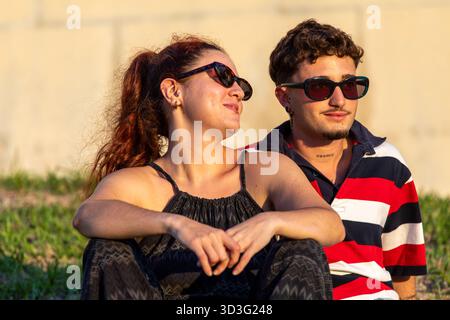 Ein Paar sitzt zusammen im Freien, sonnt sich im warmen Sonnenlicht, trägt Sonnenbrille und legere Kleidung und genießt einen entspannten und intimen Moment in Th Stockfoto