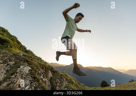Ein Mann läuft während des Sonnenaufgangs auf einem felsigen Pfad in den Pyrenäen. Das leuchtende Morgenlicht beleuchtet die Berge und hebt Hi hervor Stockfoto