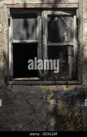Ein rustikales, verwittertes Fenster eines verlassenen Gebäudes mit abblätternder Farbe und gerissenem Holz. Schatten spielen über die alte Oberfläche und heben deren hervor Stockfoto
