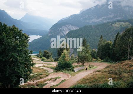 Panoramablick auf einen gewundenen Weg in den italienischen Dolomiten, umgeben von üppigen grünen Bäumen und majestätischen Bergen. Ein friedlicher See ist im d Stockfoto