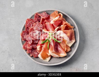 Teller mit geschnittener trockener spanischer Wurst und Prosciutto auf grauem Tischhintergrund, Draufsicht Stockfoto