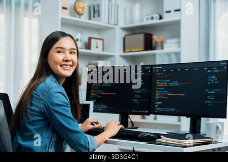 Junger asiatischer IT-Entwickler, der in die Kamera schaut, um Online-Informationen über den pc mit Programmier-Datenanwendung zu präsentieren, mit Jeansshirt Stockfoto