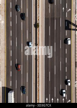 Aus der Vogelperspektive von Fahrzeugen, die die mehrspurige Autobahn unter der hellen Sonne überqueren und Schatten auf den Asphalt werfen, Rosh HaAyin, North District, Israel. Stockfoto