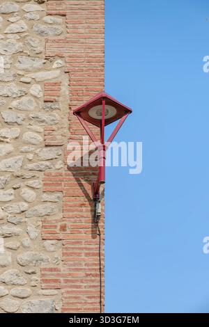 Rote Wandlampe an einem historischen Gebäude mit einer Wand aus rotem Backstein und unregelmäßigen Steinblöcken vor einem blauen Himmel Stockfoto