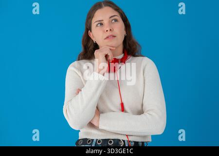 Eine nachdenkliche junge Frau mit Kopfhörern, die gegen Blau schaut Stockfoto