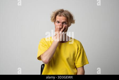 Überraschter junger Mann in gelbem Hemd, der den Mund mit der Hand während des Studioporträts bedeckt Stockfoto