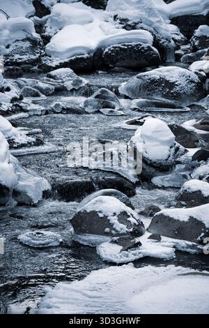 Der Fluss Jizerka fließt sanft durch eine Winterlandschaft, umgeben von eisigen Felsen und weichem Schnee. Das kalte Wasser sorgt für eine ruhige und ruhige Atmosphäre in der tschechischen Landschaft. Stockfoto
