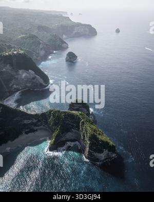 Aus der Vogelperspektive auf die zerklüftete Küste, wo türkisfarbenes Wasser auf die steilen Klippen von Nusa Penida, Bali, Indonesien trifft. Stockfoto
