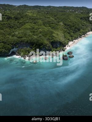 Aus der Vogelperspektive auf türkisfarbenes Wasser treffen auf die üppig grünen Klippen, die einen atemberaubenden Kontrast entlang der Küste, Bali, Indonesien, schaffen. Stockfoto